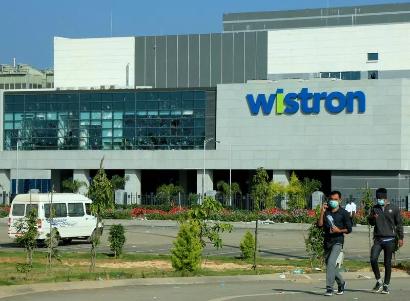 men wearing protective face masks walk past broken windows of a facility run by wistron corp a taiwanese contract manufacturer for apple in narsapura near the southern city of bengaluru india december 14 2020 reuters