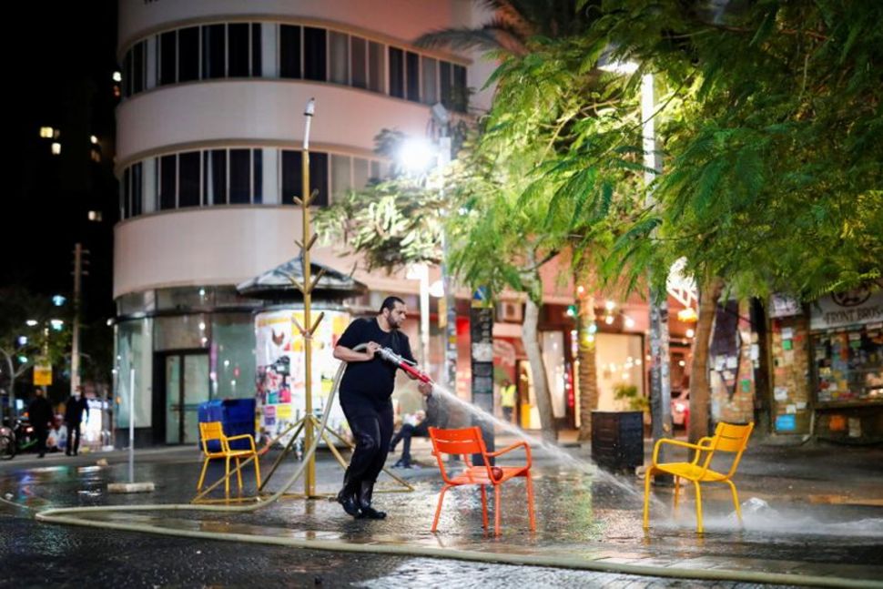 a man sprays water to clean chairs and a street as israel imposes a third national lockdown to fight climbing coronavirus disease covid 19 infections in tel aviv israel december 27 2020 reuters