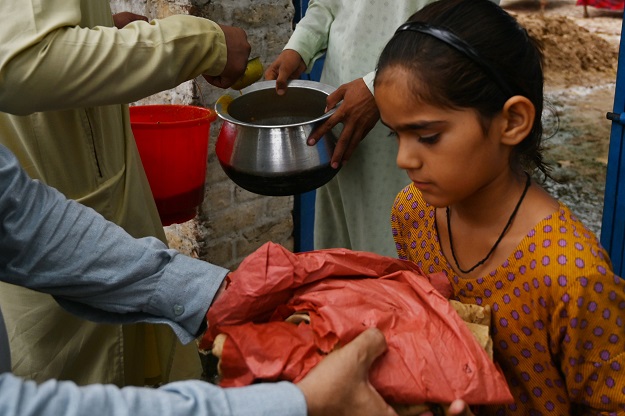 Men distribute food aid to a young girl in an earthquake-hit area. PHOTO: AFP