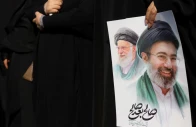 a woman holds an image of iran s new supreme leader mojtaba khamenei alongside late iranian supreme leader ayatollah ali khamenei during a funeral ceremony for the iranian military commanders who were killed in strikes amid the u s  israeli conflict with iran in tehran iran march 11 2026 majid asgaripour wana west asia news agency via reuters