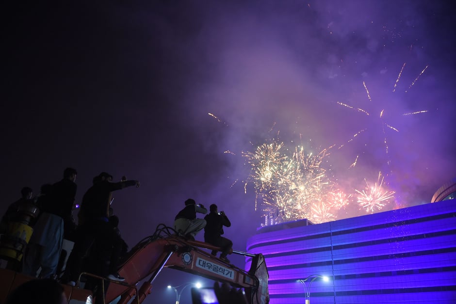 People sit on a excavator to take pictures with their smartphones as fireworks explode during the New Year celebrations in Rawalpindi. PHOTO: AFP