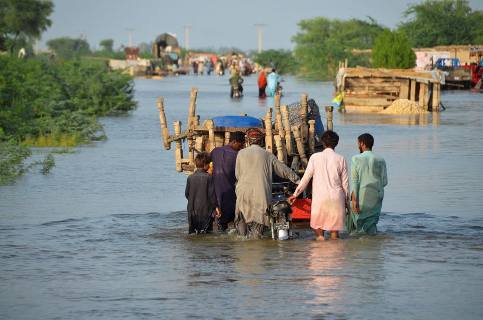 men walk along a flooded road with their belongings following rains and floods during the monsoon season in sohbatpur pakistan august 28 2022 photo reuters