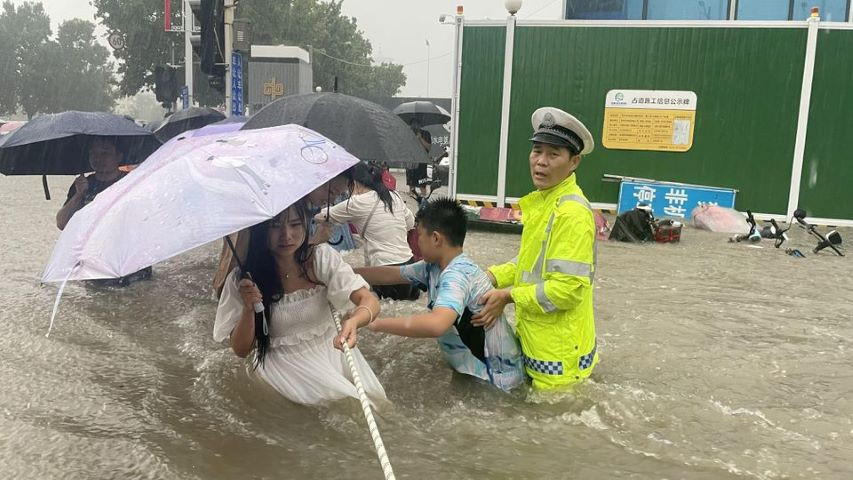 A traffic police officer guides residents to cross a flooded road with a rope during heavy rainfall in Zhengzhou, Henan province, China July 20, 2021. PHOTO: REUTERS