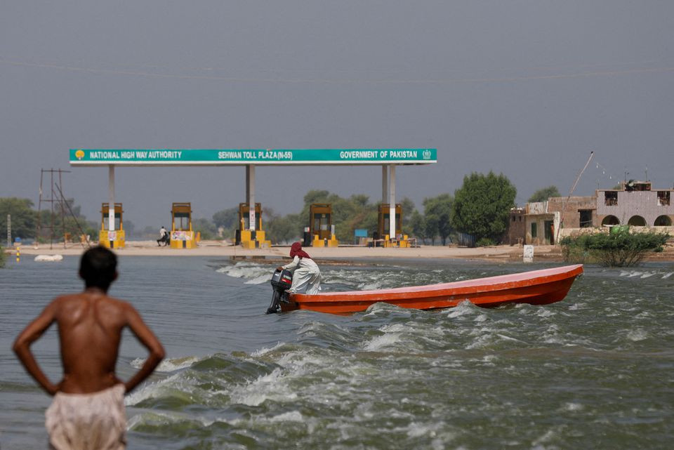 a man rides a boat past toll plaza amid flood water on main indus highway following rains and floods during the monsoon season in sehwan pakistan september 15 2022 photo reuters