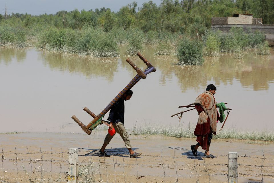 men walk with their belongings along flood waters following rains and floods during the monsoon season in charsadda august 28 2022 photo reuters