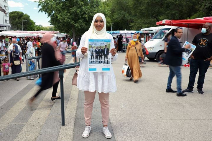 french local election candidate sara zemmahi wearing a hijab holds her campaign flyer with the slogan different but united for you as she poses during an interview for reuters ahead of the upcoming french local elections in the la mosson market in montpellier france june 5 2021 picture taken june 5 2021 reuters yiming woo