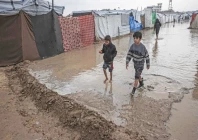 two boys walk through a waterlogged alley at a makeshift camp housing displaced palestinians in deir al balah gaza photo afp