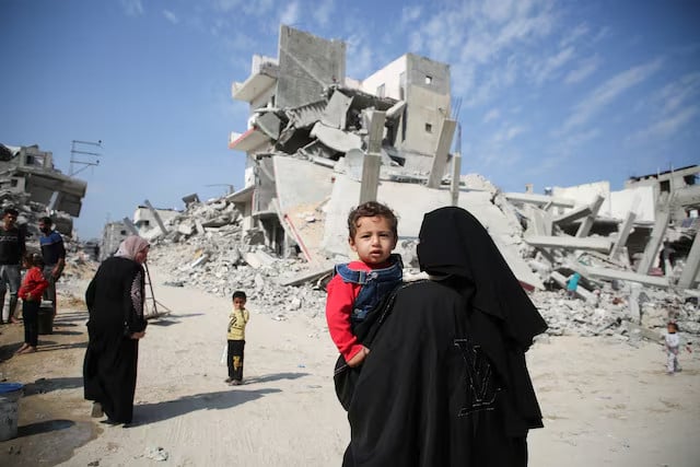 a palestinian woman carries a child as they walk past the rubble of houses destroyed in previous strikes during the israeli military offensive amid the israel hamas conflict in khan younis in the southern gaza strip november 6 2024 photo reuters