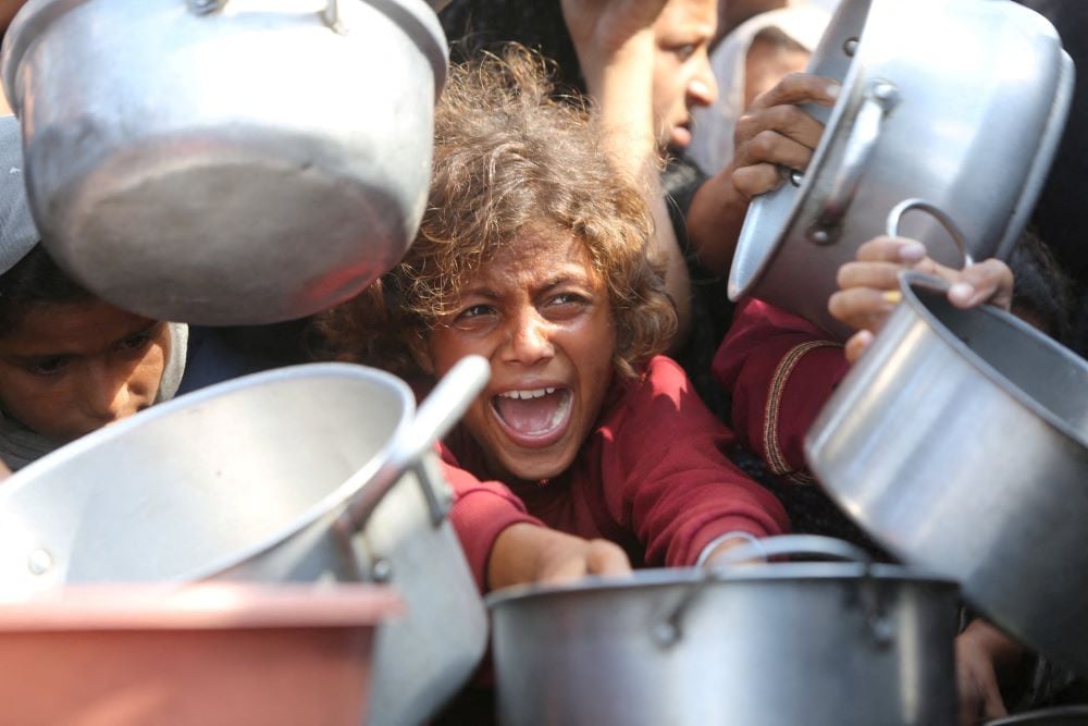 A child reacts surrounded by pots as Palestinians wait to receive food from a charity kitchen in Khan Younis, southern Gaza Strip, August 21, 2025. PHOTO:REUTERS