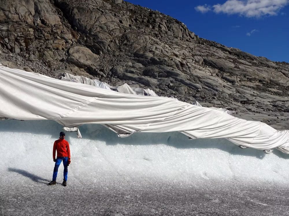 A researcher stands in front of the Rhone Glacier covered in geotextiles that protect it from accelerated melting. Source: Matthias Huss/ University of Dundee
