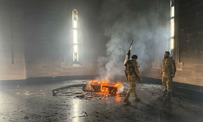 rebel fighters stand next to the burning gravesite of syria s late president hafez al assad at his mausoleum in the family s ancestral village of qardaha in the western latakia province on december 11 2024 after it was stormed by opposition factions photo afp