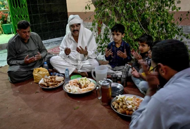 this photograph taken on february 26 2026 shows mohan lal malhi 2l a hindu caretaker of a sufi shrine breaking his fast during the islamic holy fasting month of ramadan at mithi in the tharparkar district of sindh province photo afp