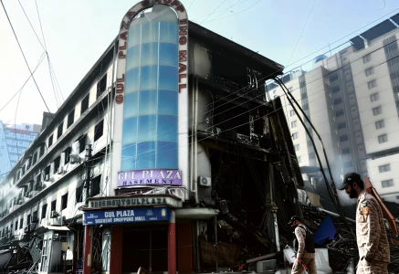 paramilitary personnel walk past charred remains of the gul plaza shopping mall in karachi on jan 22 2026 photo afp