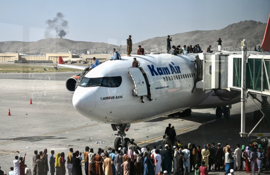 Afghan people climb atop a plane as they wait at the Kabul airport. [Photo: AFP]