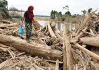 a survivor carries relief supplies while walking through tree trunks that were stranded in an area affected by a deadly flash flood following heavy rains in karang baru aceh tamiang regency aceh province indonesia december 6 2025 photo reuters