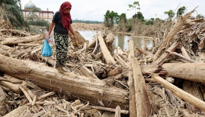 a survivor carries relief supplies while walking through tree trunks that were stranded in an area affected by a deadly flash flood following heavy rains in karang baru aceh tamiang regency aceh province indonesia december 6 2025 photo reuters