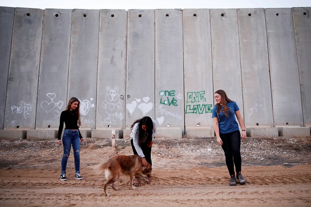 Israeli teens, Meshy Elmkies (R), 16, Liam Yefet (C), 16 and Lee Cohen, 17, co-managers of Instagram account, Otef.Gaza, play with a dog near a barrier which borders the Gaza Strip, in Kibbutz Kerem Shalom in southern Israel. PHOTO: REUTERS