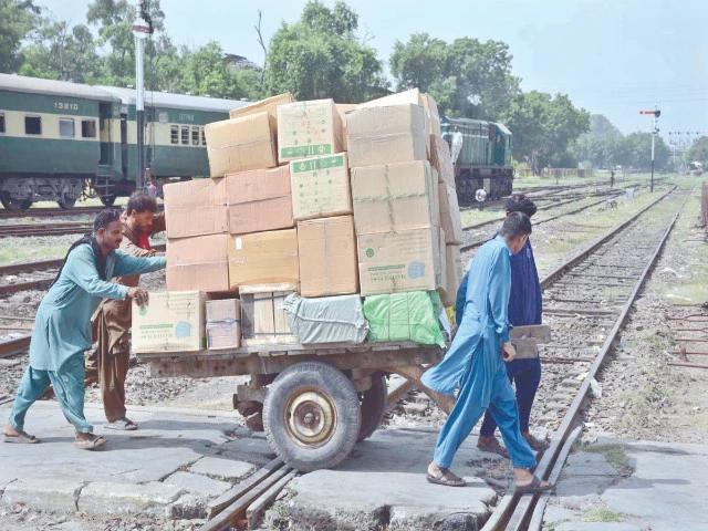 labourers push and pull a handcart loaded with goods as they cross a railway track in faisalabad photo app