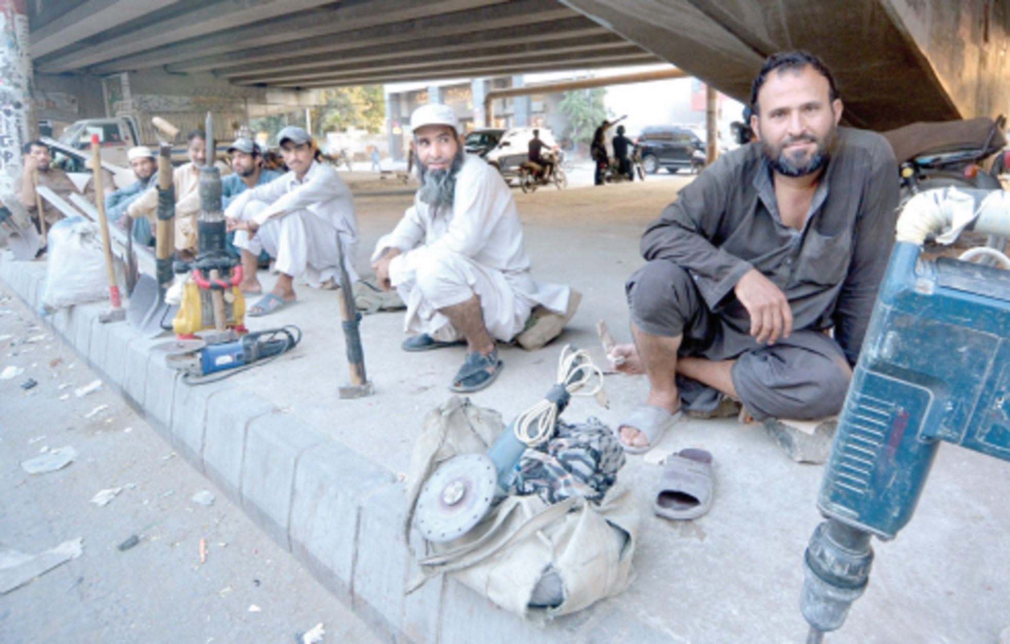 migrant workers sit on the pavement under gizri flyover waiting for someone to hire them photo jalal qureshi express