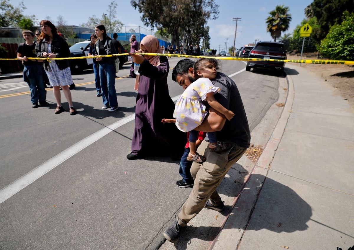 A parent passes under yellow tape cordoning an area, as he carries his child while they leave the mosque, at the scene of a shooting at the Islamic Center in San Diego, California, US, May 18, 2026.  REUTERS