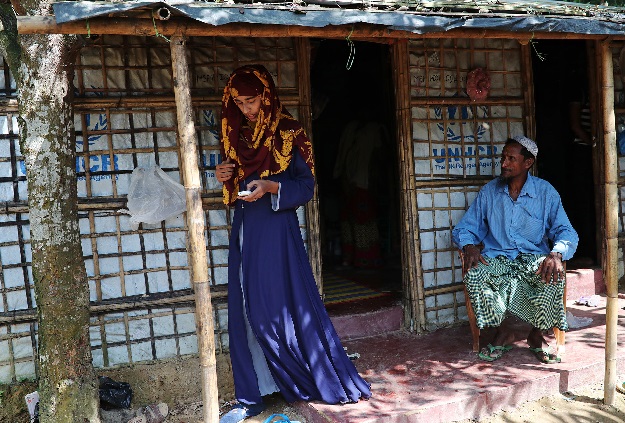 Formin checks her phone and her father waits to say goodbye before she leaves the refugee camp to attend the Asian University for Women. PHOTO: REUTERS