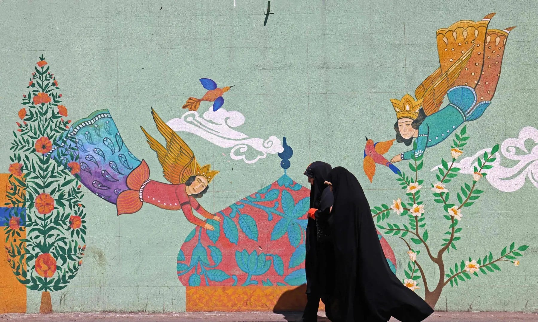 This photo taken on April 11, 2026 shows women walking past a wall mural along the roadside in Tehran. — AFP/File