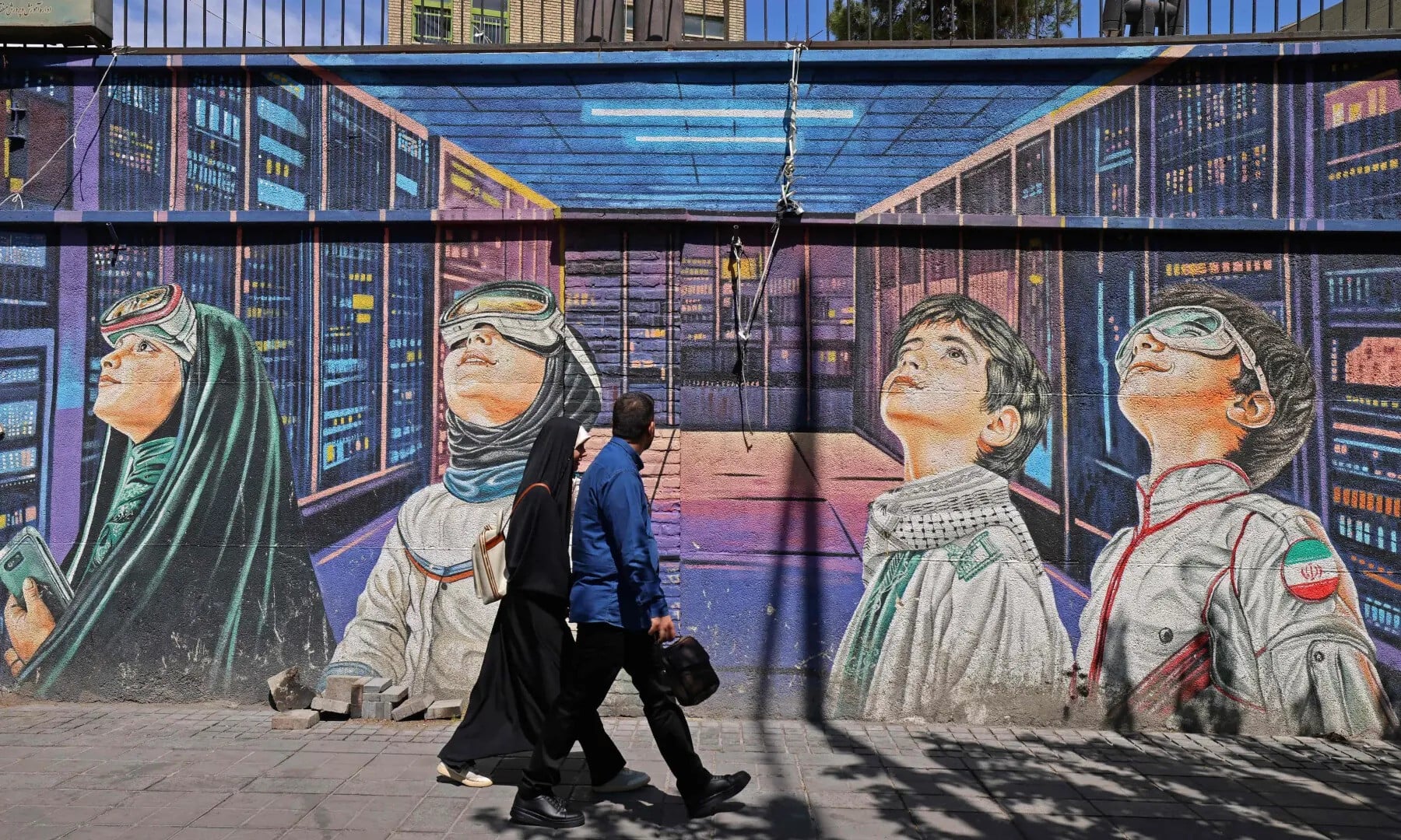 This photo taken on April 12, 2026 shows people walking past a wall mural along the roadside in Tehran. — AFP/File