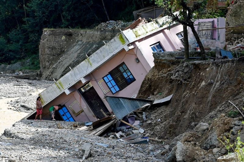 women look at a damaged building uprooted following heavy rains at a landslide affected village in lalitpur district on the outskirts of kathmandu on october 1 2024 survivors of the monsoon floods that ravaged nepal at the weekend criticised the government on october 1 for inadequate relief efforts during a disaster that killed at least 218 people photo afp