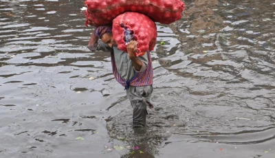 a laborer carries sacks of onions while wading through a flooded street after heavy monsoon rains in lahore on july 16 2025 photo afp