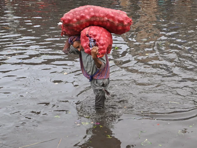 a laborer carries sacks of onions while wading through a flooded street after heavy monsoon rains in lahore on july 16 2025 photo afp a laborer carries sacks of onions while wading through a flooded street after heavy monsoon rains in lahore on july 16 2025 photo afp