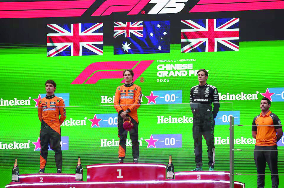 mclaren s oscar piastri stands on the podium during the national anthems after winning the chinese grand prix alongside second placed mclaren s lando norris and third placed mercedes george russell photo reuters