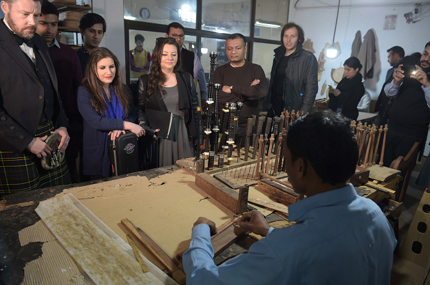 In this picture taken on January 25, 2019, a Pakistani artisan works on a machine to make components used in bagpipes as visiting international musicians observe at the Mid East bagpipe factory in the eastern city of Sialkot. PHOTO: AFP