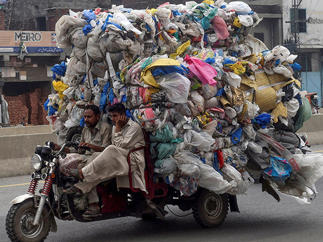 men drive a three wheeler loaded with used plastic bags in lahore photo afp