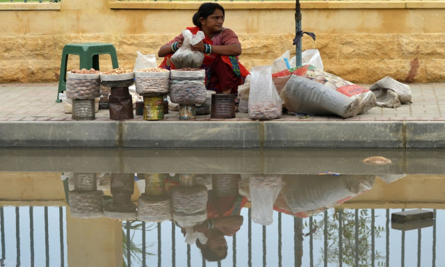 a dry fruit vendor waits for customers alongside a street inundated with rainwater in karachi photo afp a dry fruit vendor waits for customers alongside a street inundated with rainwater in karachi photo afp