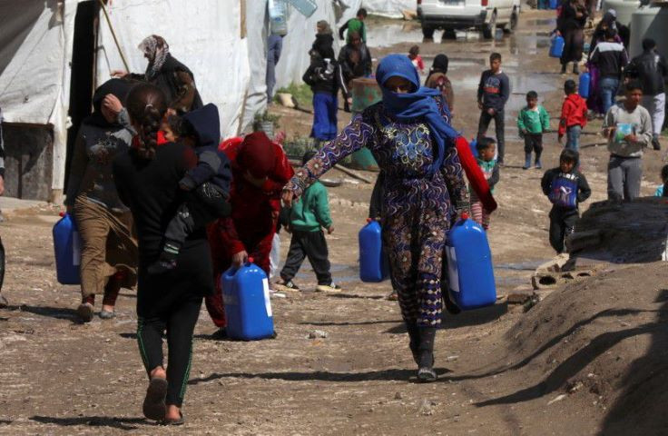 syrian refugees walk as they carry containers at an informal tented settlement in the bekaa valley lebanon march 12 2021 picture taken march 12 2021 reuters mohamed azakir file photo