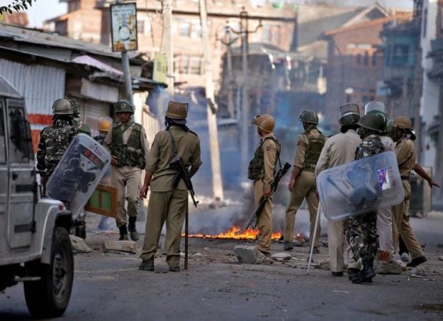 Indian policemen stand next to a burning handcart set on fire by demonstrators during a protest in Srinagar against the recent killings in Kashmir, July 18, 2016. PHOTO: REUTERS