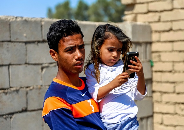 Haura, holds a cell phone as she is carried by her brother outside their family home. PHOTO: AFP