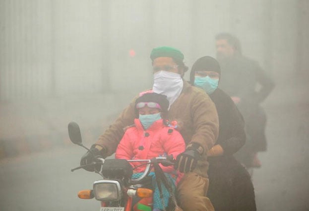 People use face masks to protect themselves from morning smog as they ride on bike along a road in Lahore. November 10, 2017. PHOTO: REUTERS