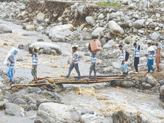 volunteers carry food medicine and other supplies for flood victims as they cross a rocky river in buner district khyber pakhtunkhwa photo afp