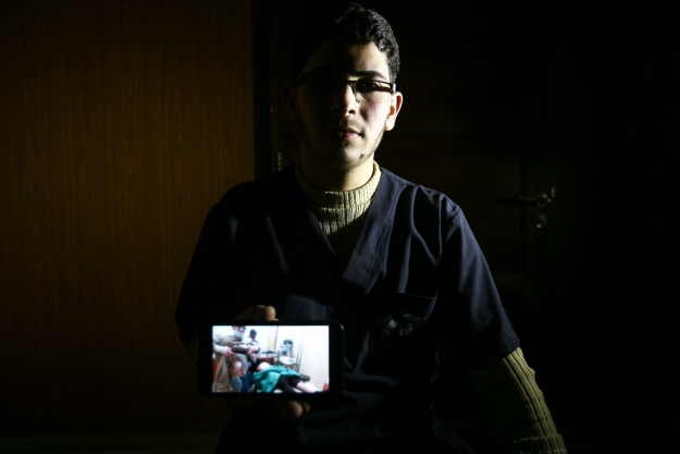 Malek Abu Jaber, a 20-year-old nurse, poses with a cell phone showing a picture of himself assisting a physician as they tend to a wounded person while he bares his own injured torso in the besieged Eastern Ghouta region on the outskirts of the capital Damascus.