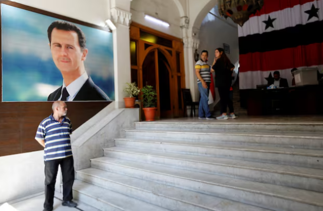 a man stands in front of a poster depicting syria s president bashar al assad at a polling station during parliamentary elections in damascus syria july 15 2024 reuters yamam al shaar purchase licensing rights