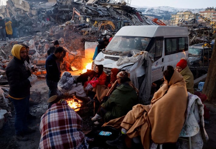 People sit around a fire next to rubble and damages near the site of a collapsed building in the aftermath of an earthquake, in Kahramanmaras, Turkey, February 8, 2023. REUTERS/Suhaib Salem