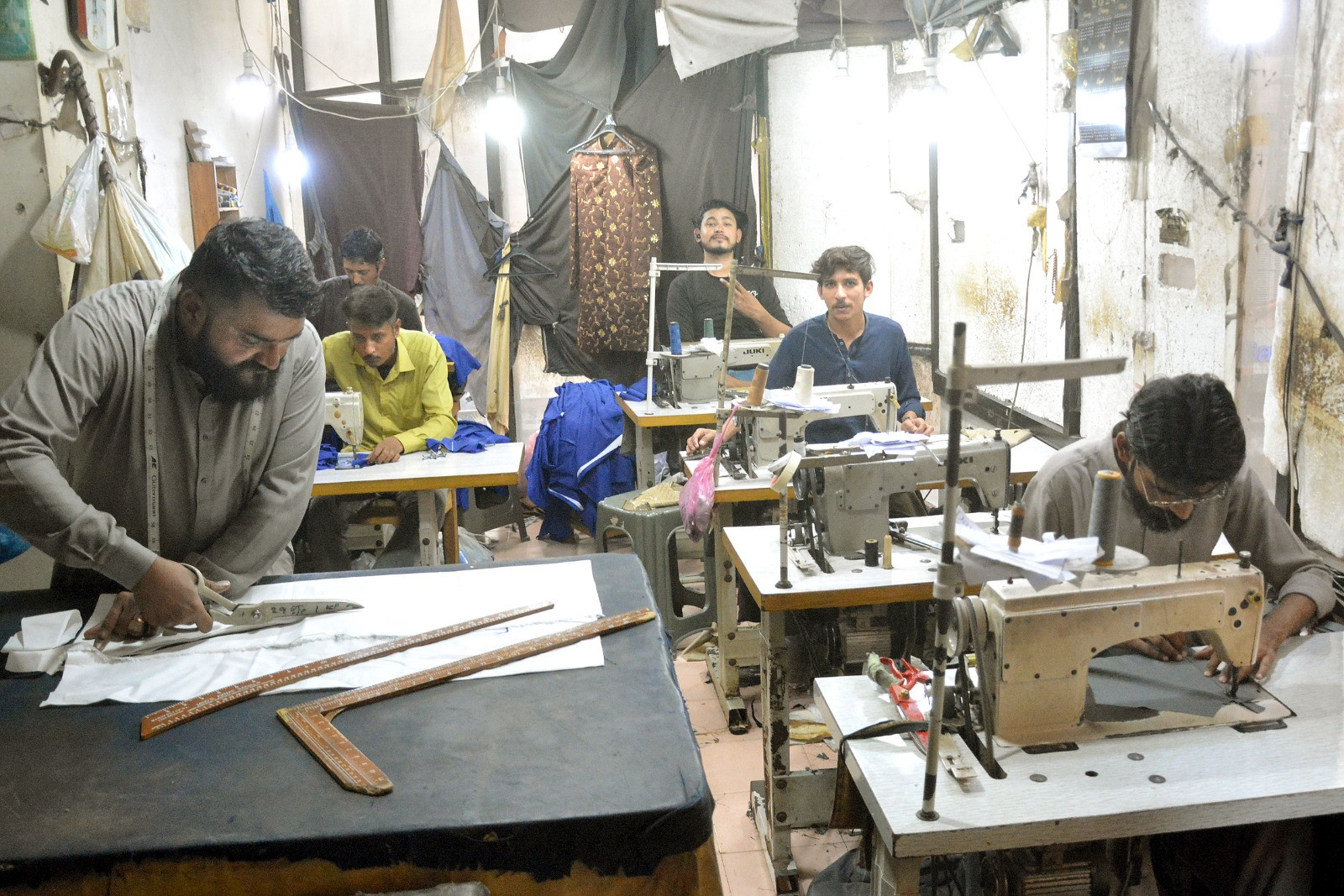 a master tailor cuts fabric while the rest of his workers sew clothes at a tailoring workshop at a commercial centre in karachi photo express