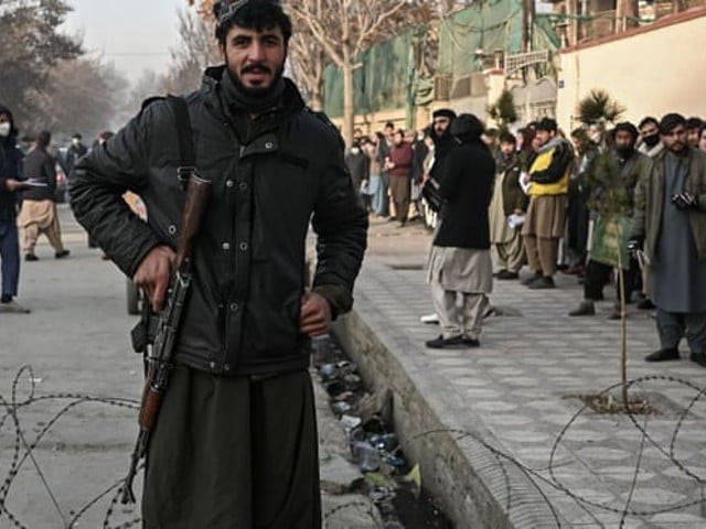a taliban fighter stands guard at a checkpoint as people queue to enter the passport office in kabul photo afp file