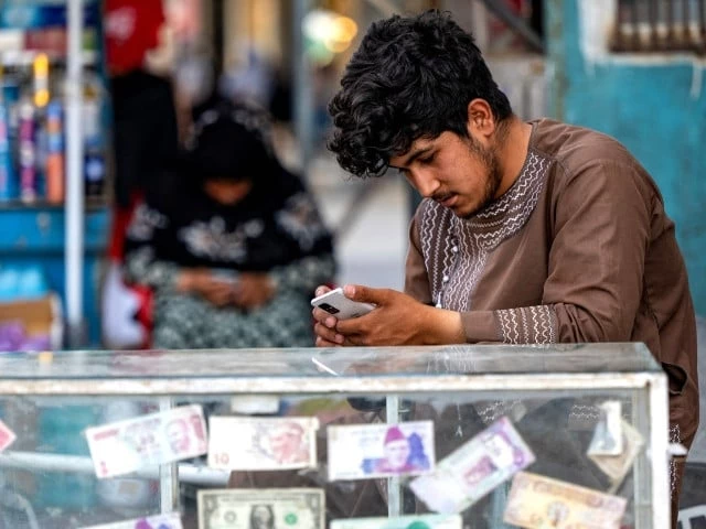 an afghan money changer checks a smartphone at his foreign currency kiosk along a road in kabul on june 18 2025 photo afp an afghan money changer checks a smartphone at his foreign currency kiosk along a road in kabul on june 18 2025 photo afp