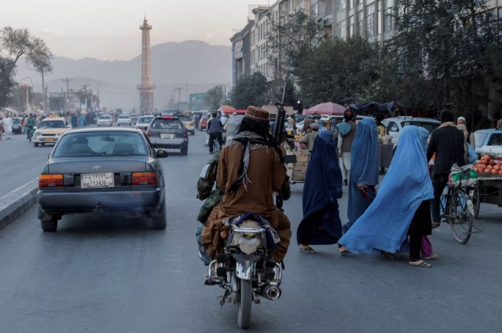 a group of women wearing burqas crosses the street as members of the taliban drive past in kabul afghanistan october 9 2021 reuters jorge silva file photo