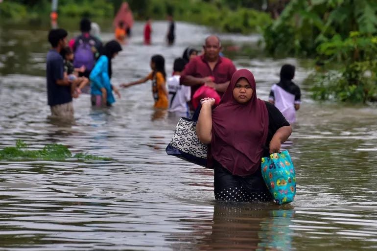 a woman wades through thigh deep waters with some of her belongings photo afp