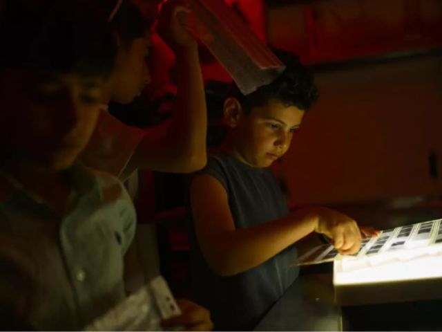 Children look at film in a darkroom during a workshop organized as part of the