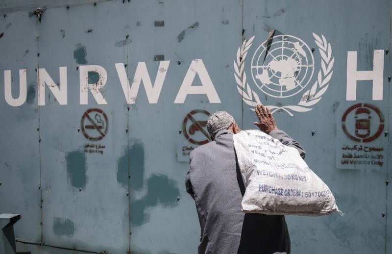 a file picture shows a palestinian man standing in front of the emblem of the un agency for palestinian refugees outside its offices in gaza city