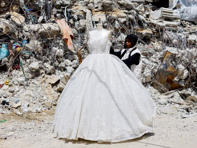 Photo: Palestinian woman looks at a wedding dress displayed outside a shop next to a pile of rubble/Reuters